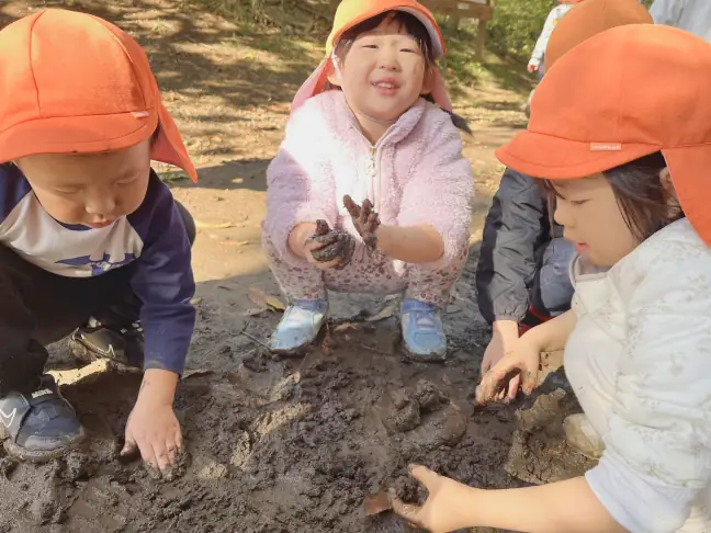 泥に手を触れ『やわらかい』『つめたーい！』と感触を言葉にする園児たち