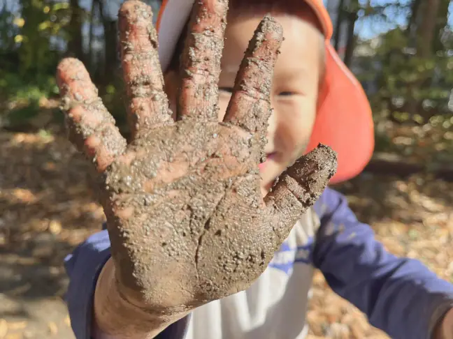泥だらけの手を『みてみて〜！』と友達に見せながらはしゃぐ園児
