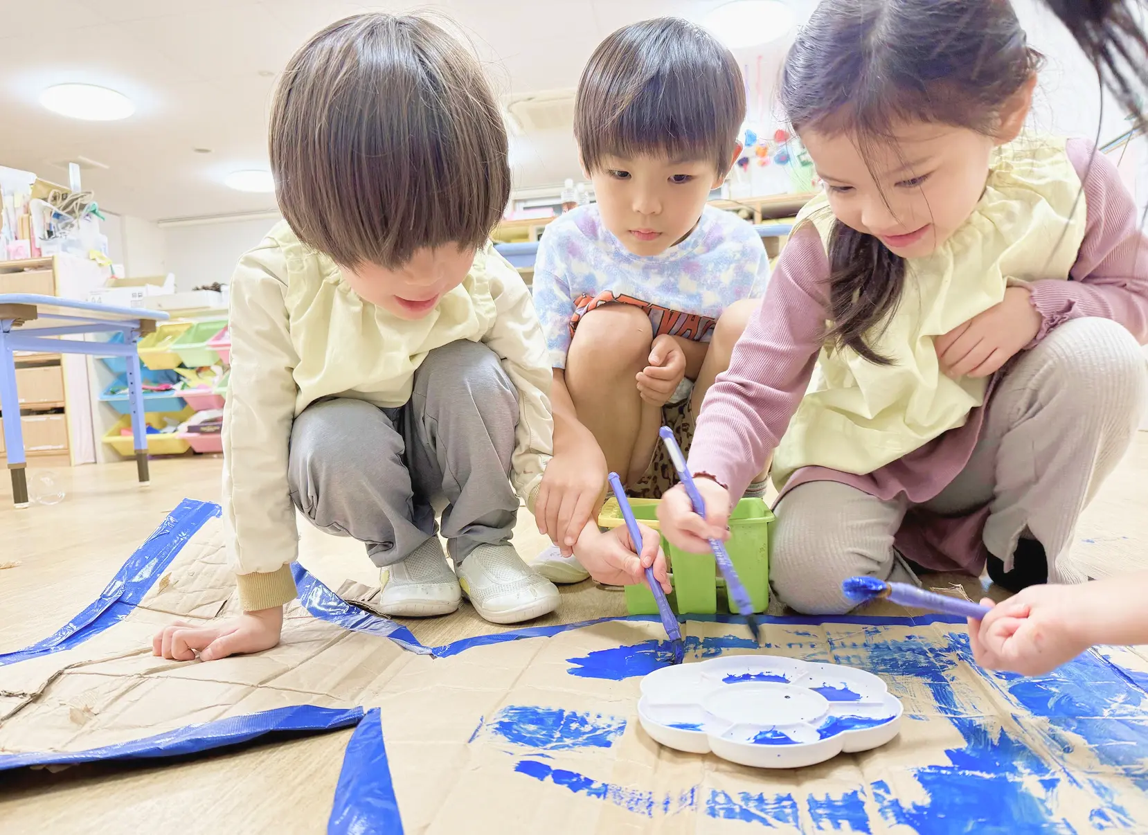ダンボールに絵の具を塗りながら自由にものづくりを楽しむ3人の子どもたち|協力し合う中で豊かな心と生きる力を育む保育園の姿