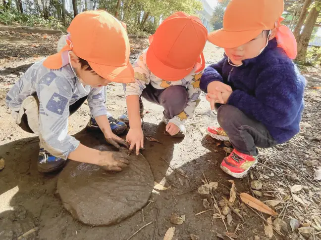泥を丸めて大きくしたり弾ませたりしながら、友達と夢中で遊ぶ子どもたち